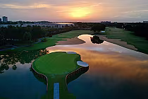 Aerial view of Hawks Landing Golf Course at sunset, featuring a green island with a bridge, water hazards, and lush fairways.