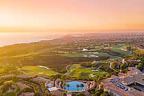 Aerial view of The Resort at Pelican Hill featuring a luxurious pool, lush golf course, and scenic coastline at sunset.