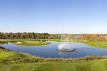 Scenic view of Hawk Ridge Golf Club with a pond, fountain, lush green fairways, and trees under a clear blue sky.