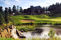 Scenic view of a golf course with a pond, waterfall, sand trap, lush green grass, and a clubhouse in Quebec, designed by a Masters champion.