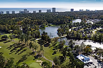 Aerial view of Arcadian Shores golf course in Myrtle Beach, with lakes, trees, residential homes, and high-rise buildings in the background.