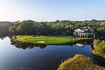 A scenic golf course with a green surrounded by water, trees, and a large Old South-style clubhouse in the background.