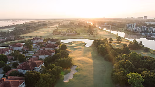 Aerial view of Grande Dunes Resort Course at sunrise, showcasing lush golf greens, water hazards, residential homes, and surrounding trees.