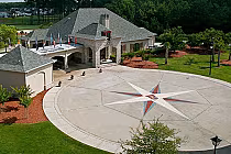 Aerial view of the International Club in Myrtle Beach featuring a large compass rose on the driveway, surrounded by lush greenery and a clubhouse with flags.