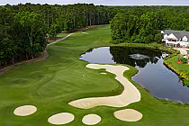 A scenic golf course with green fairways, sand bunkers, a water hazard, and a clubhouse in the background, surrounded by trees.