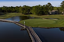A scenic golf course with a bridge over water, green fairways, trees, and a clubhouse in the background at Willbrook Plantation.