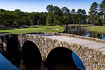 Scenic golf course with stone bridges, water hazards, lush green fairways, and tall trees inspired by world-famous layouts in Myrtle Beach.