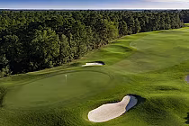 Aerial view of a lush golf course with a green, sand bunkers, and a flag, surrounded by dense trees at Legends Parkland, Myrtle Beach.