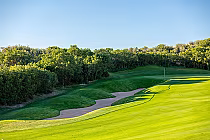 A scenic golf course with lush green fairways, sand bunkers, and a flag on the green, surrounded by trees in Denver, Colorado.