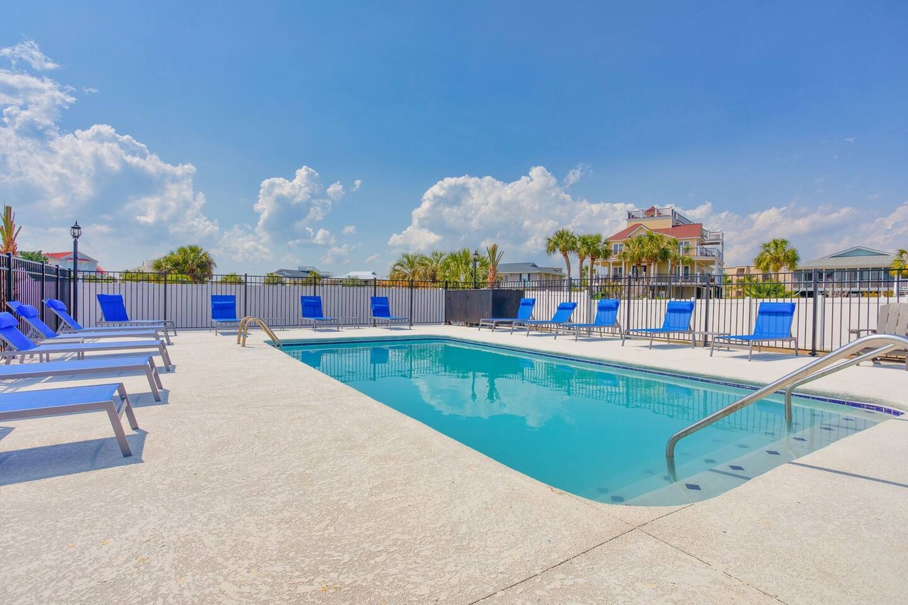 Pool Paradise Luxurious private pool area with blue lounge chairs, surrounded by a black fence, under a bright blue sky with clouds in Myrtle Beach.