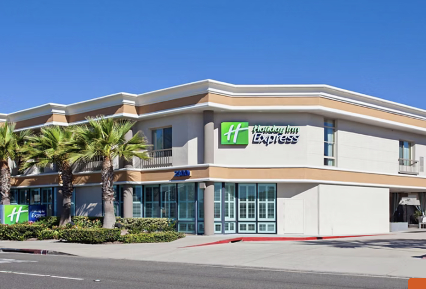 Exterior view of the Holiday Inn Express Newport Beach hotel with palm trees, clear blue sky, and hotel signage visible.