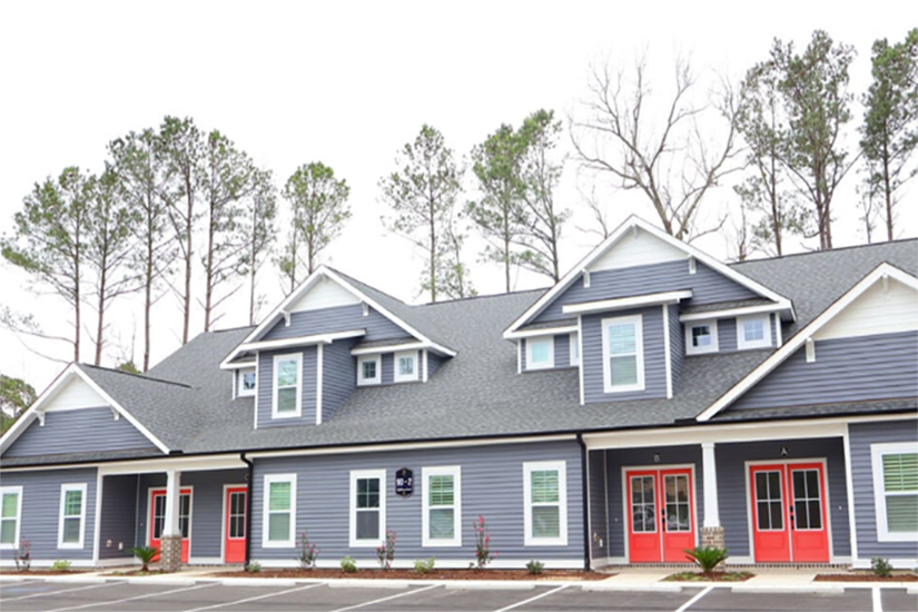 Sea Trail Golf Resort Modern blue and white townhomes at Sea Trail Golf Resort with red doors, multiple windows, and a parking lot in front.