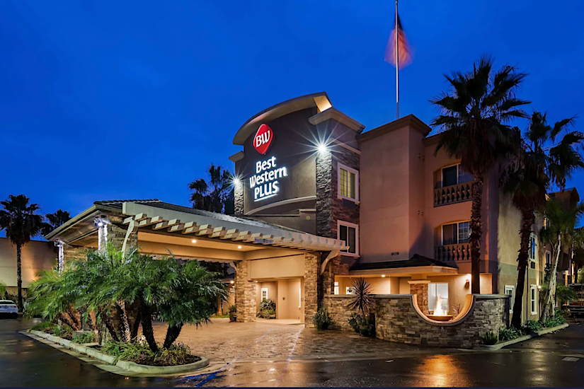 Night view of Best Western Plus Oceanside Palms hotel with illuminated sign, palm trees, and a clear evening sky.