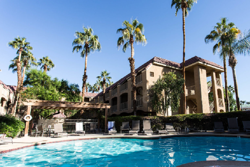 Best Western Plus Palm Desert Resort Pool area at Best Western Plus Palm Desert Resort with lounge chairs, palm trees, and a building in the background.
