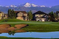 Scenic view of Colorado National Golf Club with a green, sand bunkers, a water hazard, residential houses, and snow-capped mountains in the background.