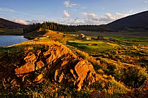 Scenic view of Keystone Ranch Golf Course in Colorado with lush green fairways, rustic buildings, and surrounding mountains at sunset.