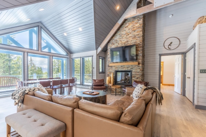 Spacious living room with large windows, modern decor, stone fireplace, and scenic mountain views in a luxury vacation home.