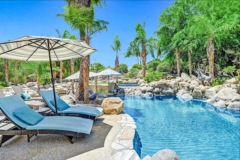 Palm Villa - Palm Desert, CA Luxury pool area at Palm Villa in Palm Desert, CA, with lounge chairs, umbrellas, lush greenery, and a putting green.