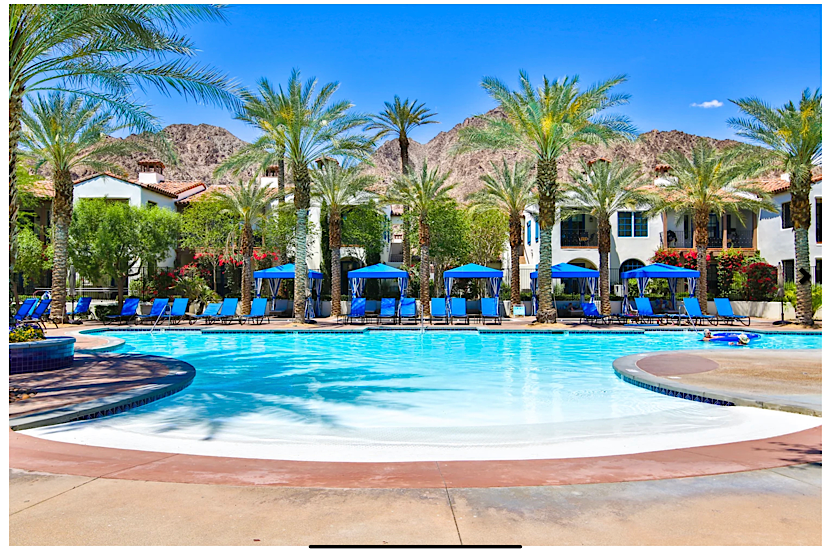 LEGACY VILLAS RESORT LA QUINTA Luxurious poolside villa at Legacy Villas Resort La Quinta with palm trees, blue lounge chairs, and mountain views.
