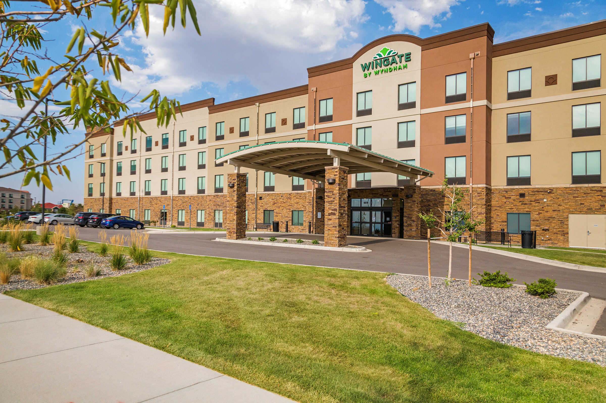 Exterior view of Wingate by Wyndham Denver Airport hotel with a parking lot, landscaped area, and a blue sky.