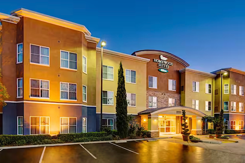 Exterior view of Homewood Suites by Hilton Carlsbad-North San Diego County at dusk, with colorful building lights and a clear sky.