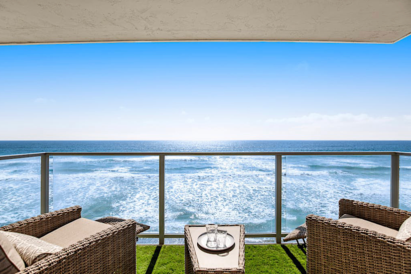 Balcony view of the ocean with wicker chairs, a small table with glasses, overlooking the waves at Buccaneer Beach Duo in Oceanside, CA.