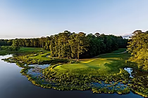 A scenic view of the RTJ Grand National Links golf course with lush green fairways, water hazards, and tall trees under a clear sky.