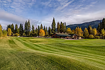 Scenic view of Whitehawk Ranch Golf Club with lush green fairways, surrounded by tall trees and mountains under a partly cloudy sky.