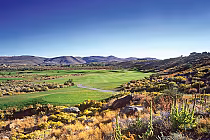 Scenic view of Wolf Run Golf Club with lush green fairways, surrounded by desert landscape and rolling hills under a clear blue sky.