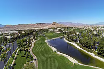 Aerial view of Rhodes Ranch Golf Club in Las Vegas, featuring a lush green golf course, water hazards, palm trees, and surrounding residential area.