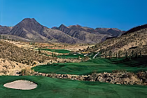 Scenic view of the Revere Golf Club's Lexington Course with lush green fairways, sand traps, and mountainous desert landscape under a clear blue sky.