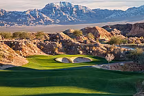 Scenic view of Conestoga Golf Club in Mesquite with a lush green fairway, sand bunkers, rocky terrain, and mountains in the background.