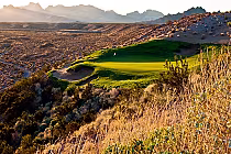 Scenic view of Laughlin Ranch Golf Club with lush green course on a hillside, desert landscape, and mountains in the background.