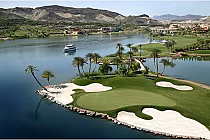 Aerial view of Reflection Bay Golf Club with a green, sand bunkers, palm trees, water, and a boat on Nevada's only Jack Nicklaus Signature course.