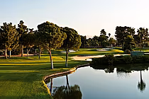 Scenic view of Las Vegas National Golf Course with lush green fairways, trees, sand traps, and water hazards under a clear sky.
