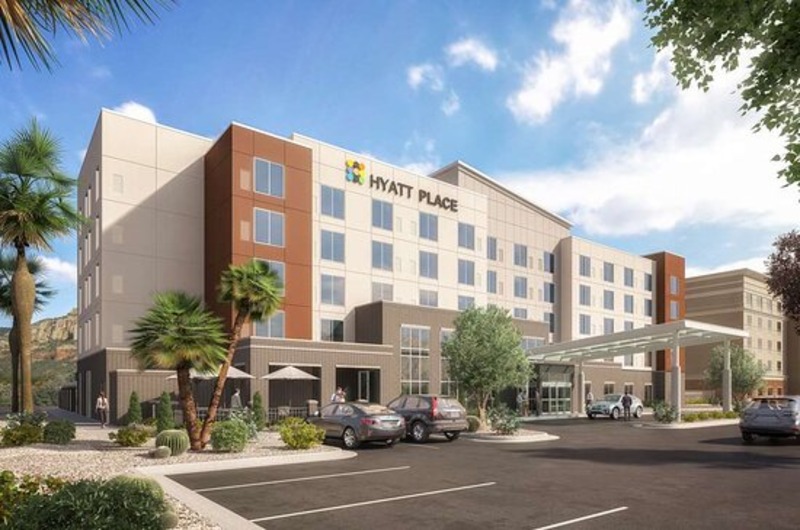 Hyatt Place St George Exterior view of Hyatt Place St George hotel with modern architecture, parking lot, palm trees, and a bright blue sky.