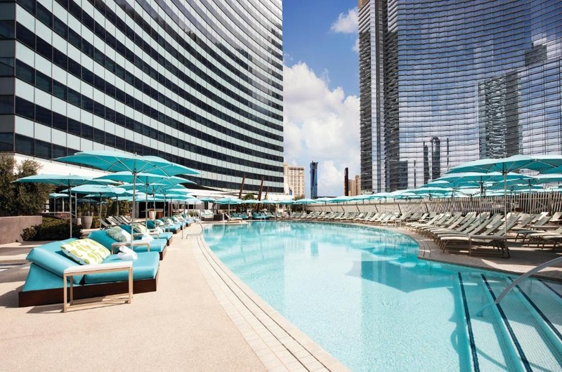 Vdara Hotel & Spa at Aria Las Vegas Luxury rooftop pool at Vdara Hotel & Spa in Las Vegas with lounge chairs, umbrellas, and city skyscrapers in the background.