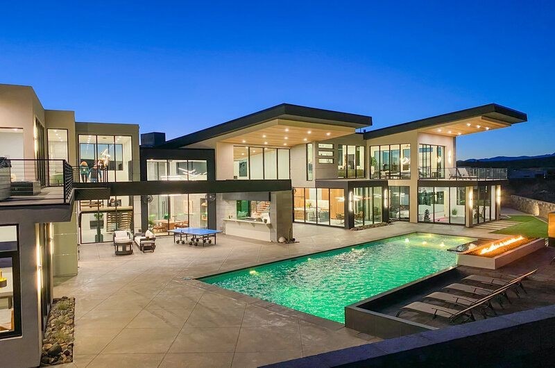 Modern luxury vacation house in Utah with large glass windows, outdoor pool, and stylish lighting at dusk.