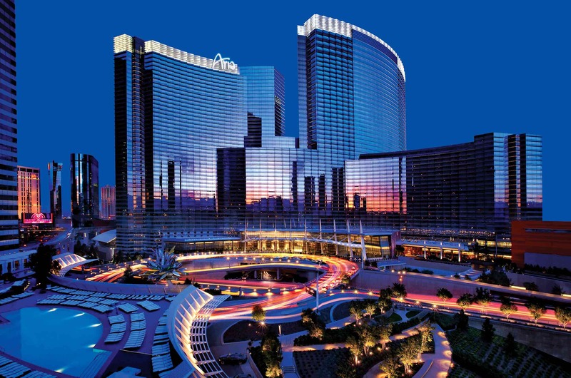 Night view of Aria Resort & Casino with illuminated modern skyscrapers, outdoor pool, and landscaped gardens.