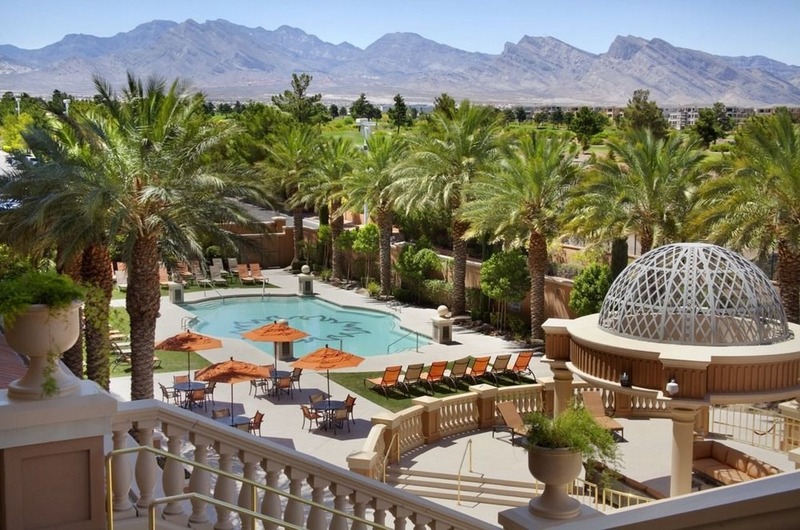 Suncoast Hotel & Casino Luxurious hotel pool area with palm trees, orange umbrellas, lounge chairs, and mountain views at Suncoast Hotel & Casino in Las Vegas.