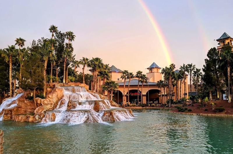 Casablanca Resort and Casino in Mesquite, Nevada, featuring a waterfall, palm trees, a large building, and a rainbow in the sky.