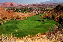 Lush green golf course with rolling fairways surrounded by desert hills and mountains, under a clear sky.