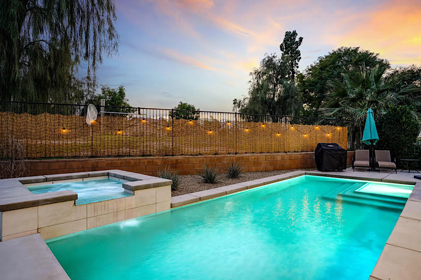 Sunset Oasis: Indio, CA A backyard pool and hot tub at sunset in Indio, California, with outdoor seating, string lights, and lush trees.