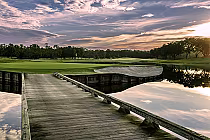 Scenic view of Evermore Cypress golf course in Orlando, Florida, featuring a wooden dock, water hazard, green fairways, and a colorful sky at sunset.