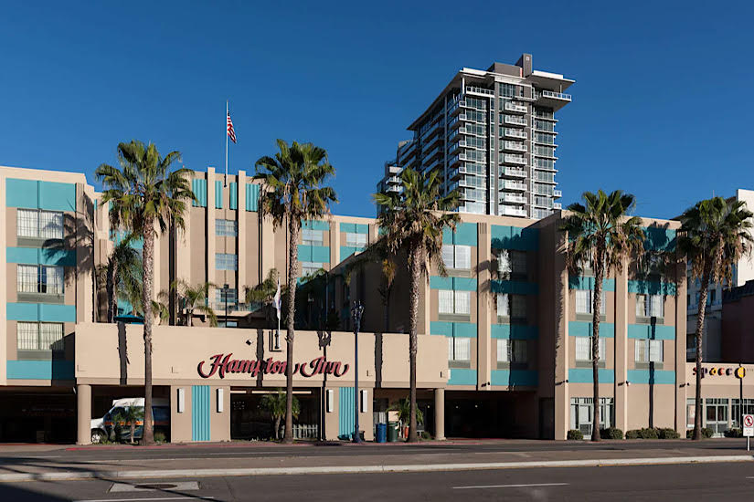 Luxury Hampton Inn in Downtown San Diego with a pool, gym, palm trees, and a tall building in the background under a clear blue sky.