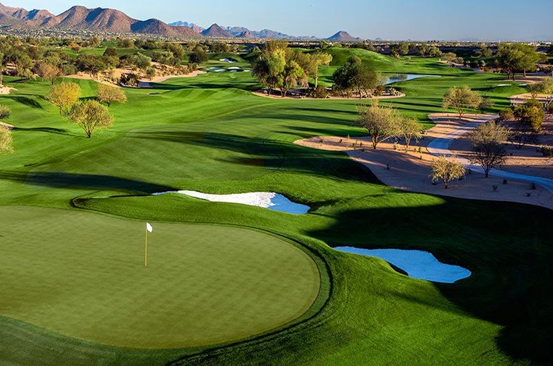 Scenic golf course in Phoenix/Scottsdale, AZ with lush green fairways, sand traps, water hazards, and mountain views in the background.