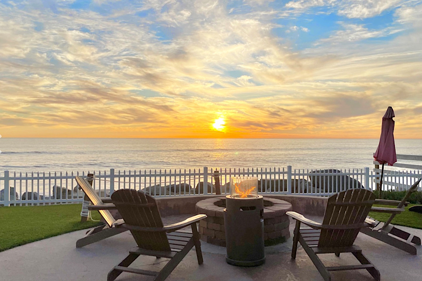 Beachfront patio with Adirondack chairs, fire pit, and ocean view during sunset in Oceanside, ideal for a luxury golf vacation.