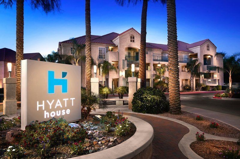 Luxurious Hyatt House Suites in Scottsdale with palm trees, vibrant landscaping, and a welcoming hotel sign at dusk.