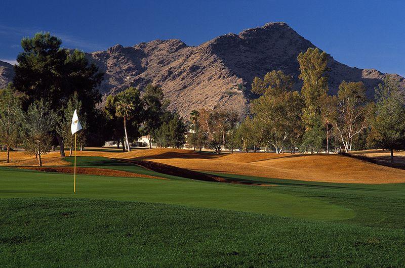 Scenic golf course in Scottsdale with lush green fairways, trees, mountains in the background, under a clear blue sky.