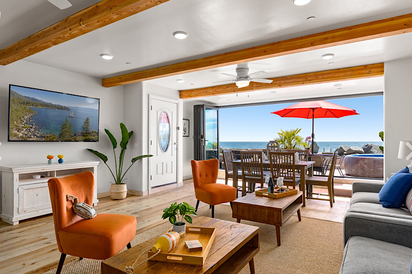 Beachfront rental living room with ocean views, featuring a dining area with a red umbrella, cozy seating, and modern decor.